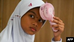 Seorang murid sekolah dasar menggunakan kipas portabel untuk mengusir hawa panas saat belajar di kelas, di Banda Aceh, Aceh, 15 Mei 2023. (Foto: Chaideer Mahyuddin/AFP)