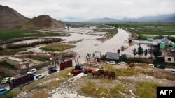 Warga Afghanistan berkumpul di sepanjang jalan menuju daerah banjir antara Samangan dan Mazar-i-Sharif menyusul banjir bandang yang disebabkan oleh hujan lebat di distrik Feroz Nakhchir, Provinsi Samangan pada 11 Mei 2024. (Foto: AFP)