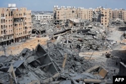 Pengungsi Palestina berjalan di tengah puing-puing rumah yang hancur akibat pemboman Israel di kawasan Hamad, sebelah barat Khan Yunis di selatan Jalur Gaza, 14 Maret 2024. (Foto: AFP)