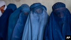 FILE - Afghan women wait to receive food distributed by a humanitarian aid group in Kabul, Afghanistan, May 23, 2023. Taliban leaders in Afghanistan have ordered fresh limitations on women, including mandating them to keep their faces and bodies covered at all times.