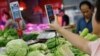 FILE - A customer scans a QR code to pay for vegetables at a morning market in Beijing, Aug. 9, 2023. Indonesia will expand QR systems in part to increase tourism from China, where that payment system is common.