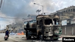 Seorang pengendara motor melewati truk tangki air yang dibakar massa di tengah bentrokan maut antaretnis di Churachandpur di negara bagian timur laut Manipur, 4 Mei 2023. (Foto: Reuters)