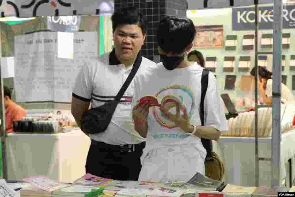 បុរស​ពីរ​នាក់​កំពុង​ឈរ​មើល​សៀវភៅ​ក្នុង​ស្តង់​សៀវភៅ​មួយកន្លែង​ក្នុង​កម្មវិធី​ពិព័រណ៌​សៀវភៅ​ក្នុង​ទិវា​ជាតិ​អំណាន​លើក​ទី​៩ នៅ​វិទ្យាស្ថានបច្ចេកវិទ្យាកម្ពុជា ក្នុង​រាជធានី​ភ្នំពេញ នាថ្ងៃទី​៩ ខែ​មីនា ឆ្នាំ​២០២៤។ (ស៊ឹម ចាន់សំណាង/វីអូអេ)