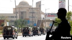 A police officer is silhouetted as he stands guard while paramilitary forces patrol as a security measure, following the visit of the Iranian President Ebrahim Raisi, in Karachi, April 23, 2024. 