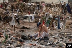 A man washes his clothes in a stream near debris left over after floodwaters devastated the village of Nanxinfang on the outskirts of Beijing, Aug. 4, 2023.
