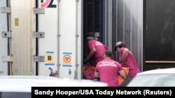 Workers in morgue operations shirts load body bags into a refrigerated trailer at Maui County Forensics Facility in Wailuku, Hawaii, Aug. 15, 2023. 