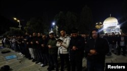 Sejumlah warga Palestina melakukan salat tarawih di area samping Masjid Al-Aqsa, Yerusalem, dengan Dome of the Rock terlihat di belakang mereka, pada 22 Maret 2023. (Foto: Reuters/Ammar Awad)