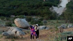 The border wall separating Jacumba Hot Springs, Calif., and Mexico is seen in the background as Chinese migrants walk to await processing by US authorities May 8, 2024, near Jacumba Hot Springs, Calif. 