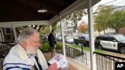 L Edward Mackouse, 80, a worshipper at the Shul at Newtown shows buttons of politicians that he favors at the synagogue guarded by a police officer in riot gear, Oct. 14, 2023 in Newtown, Pa.