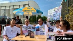 សកម្មជនចលនាមាតាធម្មជាតិចំនួន៥នាក់ ប្រមូលផ្តុំគ្នានៅក្បែរ​តុលាការ​ ខណៈកងកម្លាំងសណ្តាប់ធ្នាប់ខណ្ឌឬស្សីកែវ ដាក់ត្រួតពិនិត្យនិងរឹតបន្តឹងការចេញចូលតុលាការ នៅថ្ងៃទី១១ ខែមិថុនា ឆ្នាំ២០២៤។ (លាស់ លីបលីប/វីអូអេ)
