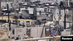 Two people examine a burned house after an inferno destroyed much of the historic Maui resort town of Lahaina, Hawaii, Aug. 13, 2023. 