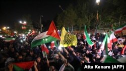 Para demonstran melambaikan bendera Iran dan Palestina saat demo di depan Kedutaan Besar Inggris di Teheran, Minggu, 14 April 2024, setelah Iran meluncurkan serangan drone dan misil ke Israel. (Foto: Atta Kenare/AFP)