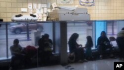 FILE - Immigrants from Venezuela are reflected in a marble wall while taking shelter at the Chicago Police Department's 16th District station on May 1, 2023.
