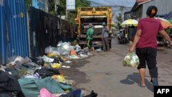 រូបឯកសារ៖ ស្ត្រីម្នាក់យក​ថង់​សំរាម​ទៅចោល ខណៈ​កម្មករ​កំពុង​ប្រមូល​សំរាម​នៅ​លើ​ដងផ្លូវ​មួយ​ក្នុង​រាជធានីភ្នំពេញ កាលពីថ្ងៃទី៣ ខែឧសភា ឆ្នាំ២០១៨។ 