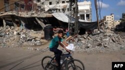 Seorang anak laki-laki Palestina menaiki sepeda melewati gedung-gedung yang hancur di Rafah, di selatan Jalur Gaza, pada 26 Mei 2024. (Foto: AFP/Eyad Baba)
