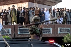 Para pria menyaksikan personel keamanan bersenjata Taliban saat konvoi kendaraan dalam parade di Kabul pada 15 Agustus 2023, saat Taliban merayakan ulang tahun kedua pengambilalihan mereka. (Foto: AFP)