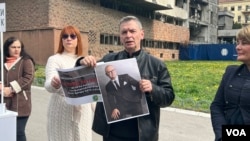 Lider Ekološkog ustanka Aleksandar Jovanović Ćuta pokazuje plakat peticije za podizanje spomen obeležja na mestu uništene zgrade Generalštaba VS i portret funkcionera vladajuće SNS Gorana Vesića, ispred zgrade Generalštaba u Beogradu, 15. marta 2024. (Foto: VoA/Rade Ranković)