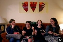 Mahasiswa Benedictine College, dari kiri: Ashley Lestone, Hannah Moore, Niki Wood, dan Madeline Hays tertawa bersama saat mereka membaca kitab doa mereka sebelum berdoa sore di sebuah kapel di rumah mereka di Atchison, Kansas, 3 Desember 2023.(AP/Charlie Riedel)