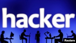 Foto ilustrasi yang menunjukkan kumpulan manusia dengan laptop dan telepon genggamnya di depan tulisan "hacker." Foto diambil pada 19 Februari 2024. (Foto: Reuters/Dado Ruvic)