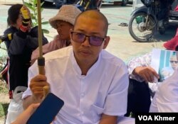 លោក យីម លាងហ៊ី អង្គុយបាំងឆ័ត្រនៅមុខរបាំងឃាំងរបស់កងកម្លាំងសន្តិសុខនៅច្រកចូលសាលាដំបូងរាជធានីភ្នំពេញ នៅថ្ងៃទី៥ ខែមិថុនា ឆ្នាំ២០២៤។ (ទឹម រក្សា/វីអូអេ)