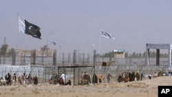 FILE - Pakistani and Taliban flags flutter on their respective sides while people walk through a security barrier to cross the Pakistan-Afghan border in Chaman, Pakistan, Aug. 18, 2021.
