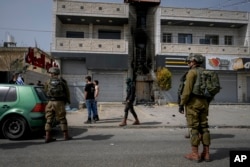 Israeli soldiers and Jewish settlers, some of them masked, stand next to a damaged Palestinian building in the town of Hawara, near the West Bank city of Nablus, Feb. 27, 2023.