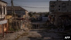 Local residents walk past damaged shops and buildings in Kupiansk, Kharkiv region, Ukraine, on Sept. 28, 2023. 