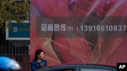 Motorists pass a woman standing near a billboard along a street in Beijing, Nov. 1, 2023.