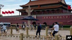 A security person watch over residents passing in front of Tiananmen Gate in Beijing, June 4, 2023.