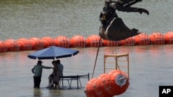 Workers take a break from deploying large buoys to be used as a border barrier along the banks of the Rio Grande in Eagle Pass, Texas, July 12, 2023. The floating barrier is being deployed in an effort to block migrants from entering Texas from Mexico.