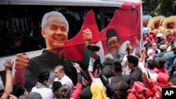 FILE - Para pendukung paslon capres-cawapres Pilpres 2024 Ganjar Pranowo dan Mohammad Mahfud, mengelilingi bus kampanye saat mendaftarkan diri di gedung Komisi Pemilihan Umum di Jakarta, 19 Oktober 2023. (AP/Achmad Ibrahim)