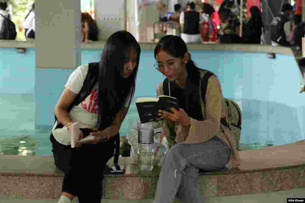 អ្នកចូលរួម​២នាក់​កំពុង​អង្គុយ​អាន​សៀវភៅ​ដែល​ទើប​នឹង​ទិញ​រួច​​កម្មវិធី​ពិព័រណ៌​សៀវភៅ​ក្នុង​ទិវា​ជាតិ​អំណាន​លើក​ទី​៩ នៅ​វិទ្យាស្ថានបច្ចេកវិទ្យាកម្ពុជា ក្នុង​រាជធានី​ភ្នំពេញ នាថ្ងៃទី​៩ ខែ​មីនា ឆ្នាំ​២០២៤។ (ស៊ឹម ចាន់សំណាង/វីអូអេ)