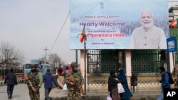 Sejumlah anggota pasukan paramilliter berjaga di dekat papan iklan yang menampilkan pengumuman kunjungan perdana Menteri India Narendra Modi ke Srinagar, Kashmir, pada 6 Maret 2024. (Foto: AP/Mukhtar Khan)