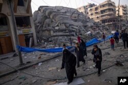 Warga Palestina berjalan di dekat reruntuhan sebuah bangunan setelah terkena serangan udara Israel, di Kota Gaza, 8 Oktober 2023. (Foto: AP)