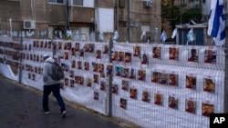 A man passes by a fence with photographs of hostages, mostly Israeli civilians who were abducted during the Oct. 7, unprecedented Hamas attack on Israel, in Ramat Gan, Israel, Nov. 22, 2023.