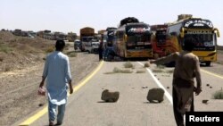 Orang-orang berjalan melewati truk pasokan yang diparkir di sepanjang jalan, setelah lalu lintas dihentikan menyusul serangan di jalan raya di provinsi Balochistan yang bergolak di Pakistan, 26 Agustus 2024. (Stringer/REUTERS)