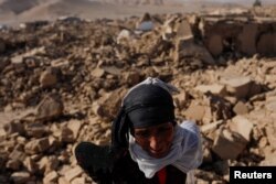 An Afghan woman stands next to her house after the recent earthquake in Chahak village in the Enjil district of Herat province, Afghanistan, Oct.11, 2023.