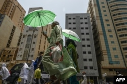 Para jemaah haji menggunakan payung untuk melindungi diri dari terik matahari saat berjalan di kota suci Mekkah pada 23 Juni 2023. (Foto: Sajjad HUSSAIN/AFP)