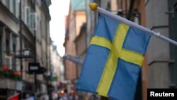 Bendera Swedia berkibar di luar sebuah toko dengan latar belakang kota tua Stockholm, Swedia, 14 Juli 2023. (Foto: REUTERS/Tom Little)