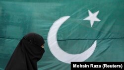 Seorang perempuan mengenakan burqa berjalan melewati bendera nasional Pakistan di Lahore 13 Agustus 2011. Pakistan mengatakan pada Rabu (17/1) bahwa Iran melakukan serangan udara di wilayahnya yang menewaskan dua anak. (Foto: REUTERS/Mohsin Raza)