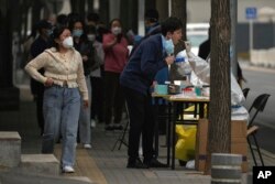 Warga mengantre untuk mengambil swab tenggorokan COVID-19 rutin mereka di tempat pengujian virus corona di sepanjang trotoar pejalan kaki di Beijing, China, 13 Oktober 2022. (Foto: AP)