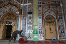 Seorang petugas menggulung sajadah dari aula utama masjid menyusul peraturan baru pemerintah untuk mengatur jarak sosial dalam upaya menekan penyebaran virus COVID-19 di Rawalpindi, 5 April 2021, menjelang bulan suci Ramadan. (Foto: Aamir QURESHI / AFP).