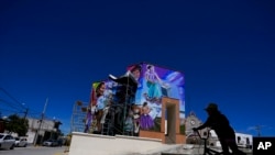 A pedestrian rides her bike in front of a mural painted by Mexican artist Jesus Rodriguez, in San Salvador, Mexico, July 30, 2022.