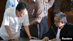 Mantan Ketua DPR Setya Novanto (kiri), tersangka kasus korupsi e-KTP, berbicara kepada pengacaranya dalam sidang pertama di Jakarta, 13 Desember 2017. (Antara Foto/Wahyu Putro via Reuters)