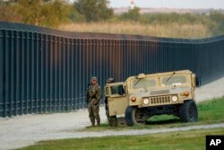 FILE - National Guardsmen stand watch over a fence near the International bridge where thousands of Haitian migrants have created a makeshift camp, in Del Rio, Texas, Sept. 18, 2021.