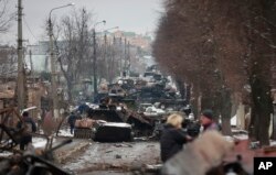 Orang-orang melihat sisa-sisa kendaraan militer Rusia yang hancur di jalan di kota Bucha, dekat Ibu Kota Kyiv, Ukraina, Selasa, 1 Maret 2022. (Foto: AP)
