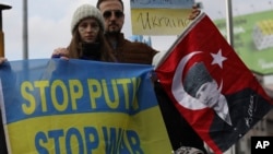 Women with their faces painted in the colors of the Ukrainian flag hold a banner and a Turkish flag with an image of Turkey's founder Mustafa Kemal Ataturk as Ukrainians, Turks and Crimean Tatars protest Russia's war in Ukraine, in Ankara, Turkey, March 5