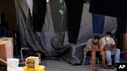 FILE - Men wait at a migrant shelter, April 21, 2022, in Tijuana, Mexico. A Trump-era policy forces asylum-seekers to wait in Mexico for hearings in U.S. immigration court. 