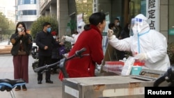 FILE - A medical worker takes a swab sample at a testing booth for coronavirus disease (COVID-19), after the government gradually loosened restrictions on COVID-19 control, in Wuhan, Hubei province, China Dec. 9, 2022.