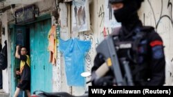 Seorang pria melihat keluar dari sebuah toko ketika seorang polisi bersenjata berjaga setelah ledakan di sebuah kantor polisi distrik, yang menurut pihak berwenang merupakan dugaan bom bunuh diri, di Bandung, Jawa Barat. (Foto: REUTERS/Willy Kurniawan)